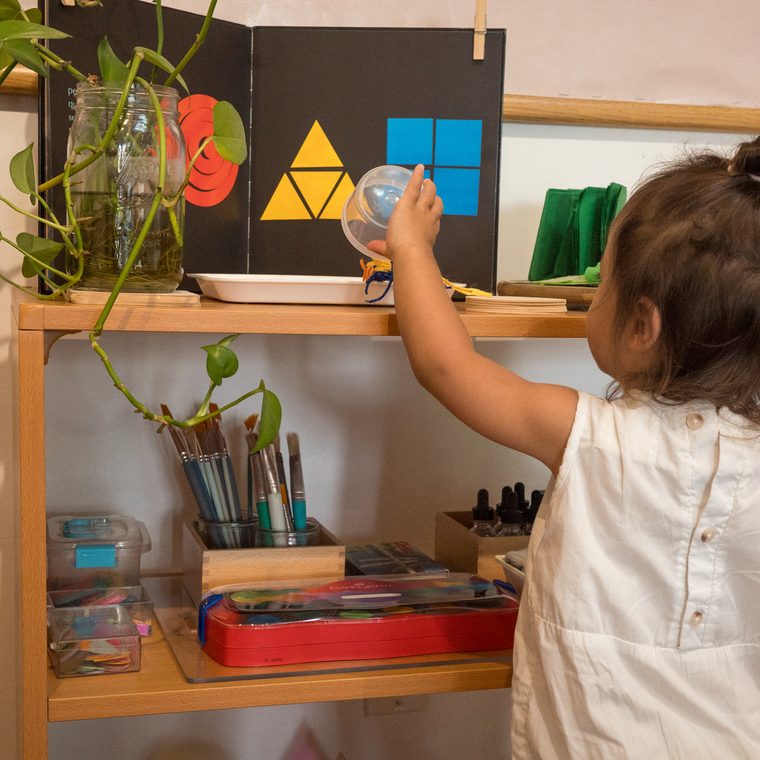 A child reaching for materials at a shelf with a shape book
