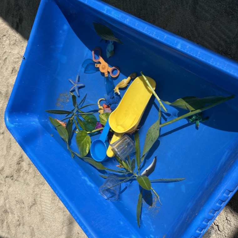 A blue water tray outdoors filled with leaves, scoops, and sea creatures for sensory play