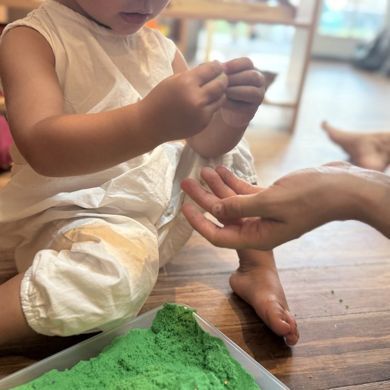 A child molding green kinetic sand on the floor