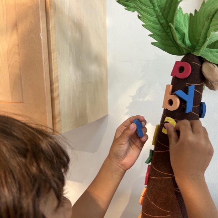 A child arranging colorful letters on a felt alphabet tree