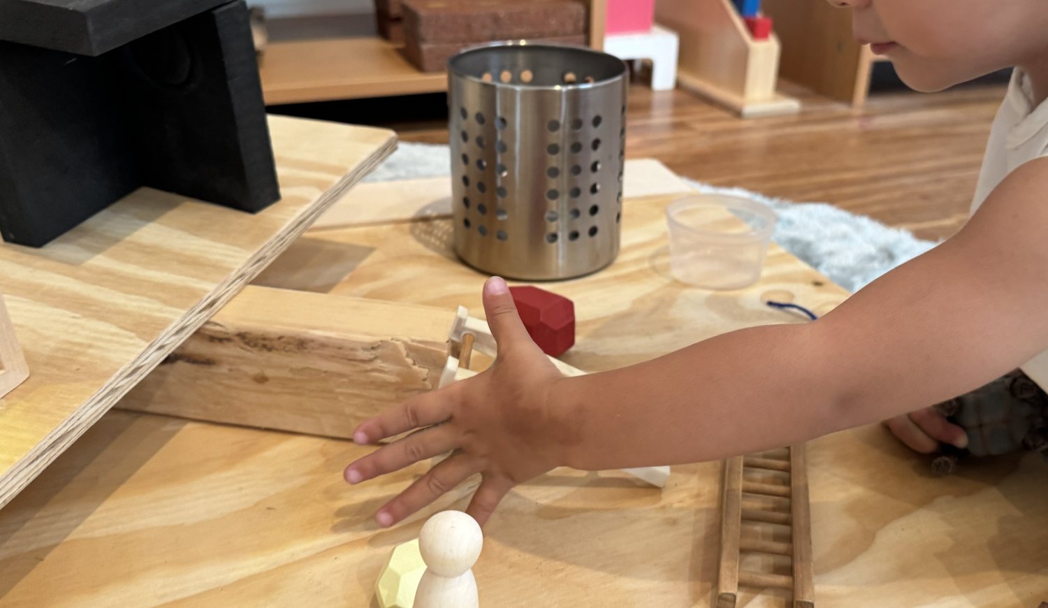 A child reaching to explore wooden blocks and loose parts on a table